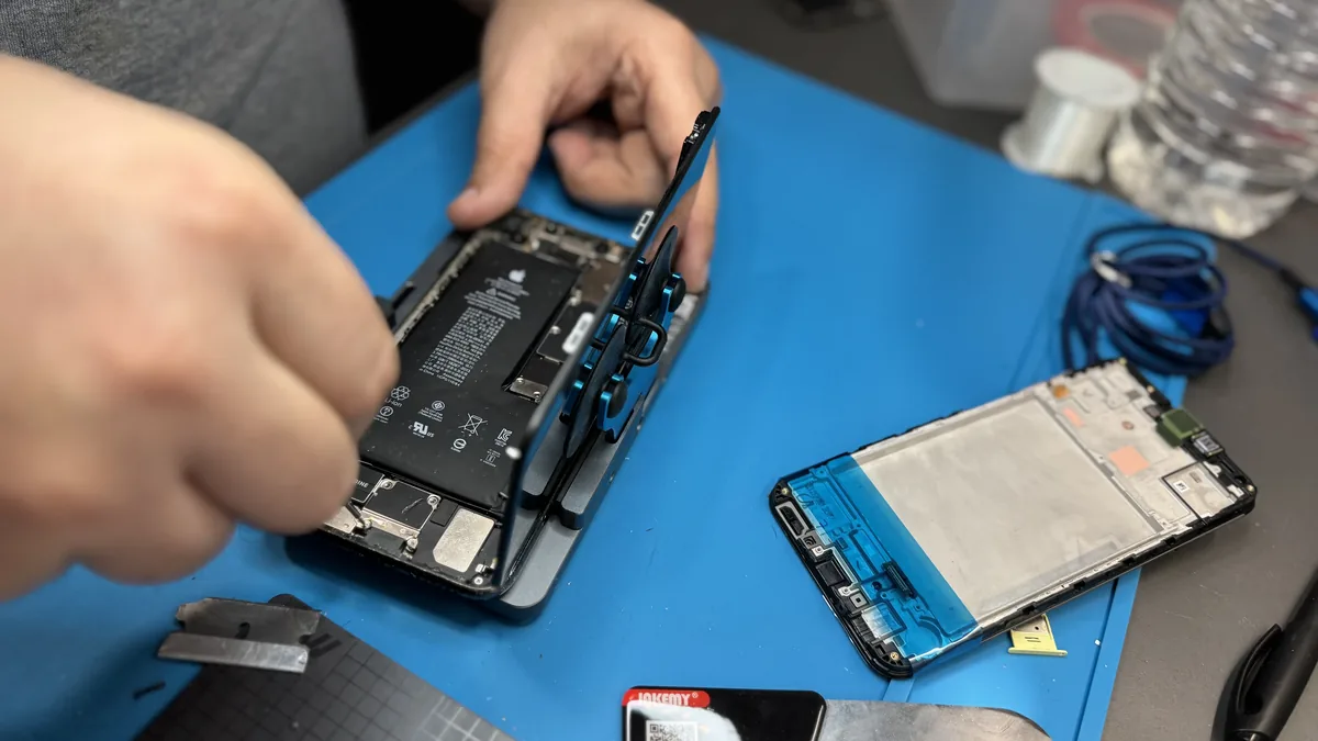Deux mains gantées démontant un smartphone à l’établi